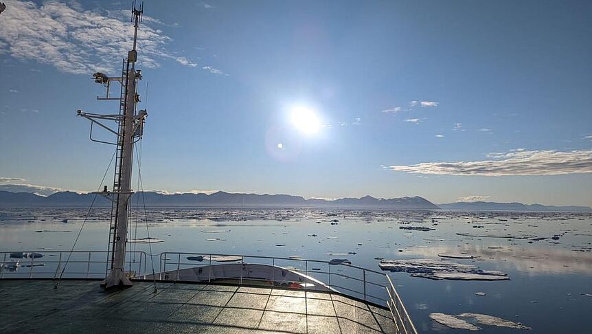 Das Schiff Maria S. Merian vor der grönländischen Ostküste bei (noch) wunderbarem Wetter. Zu sehen sind das Meer, Eisschollen und Sonnenschein