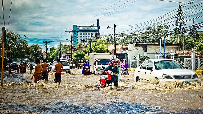 Foto von überschwemmter Straße mit Menschen, die sich durch die Fluten kämpfen
