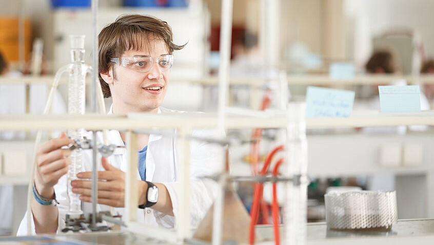 Symbolfoto von Studierendem im weißen Kittel im Labor